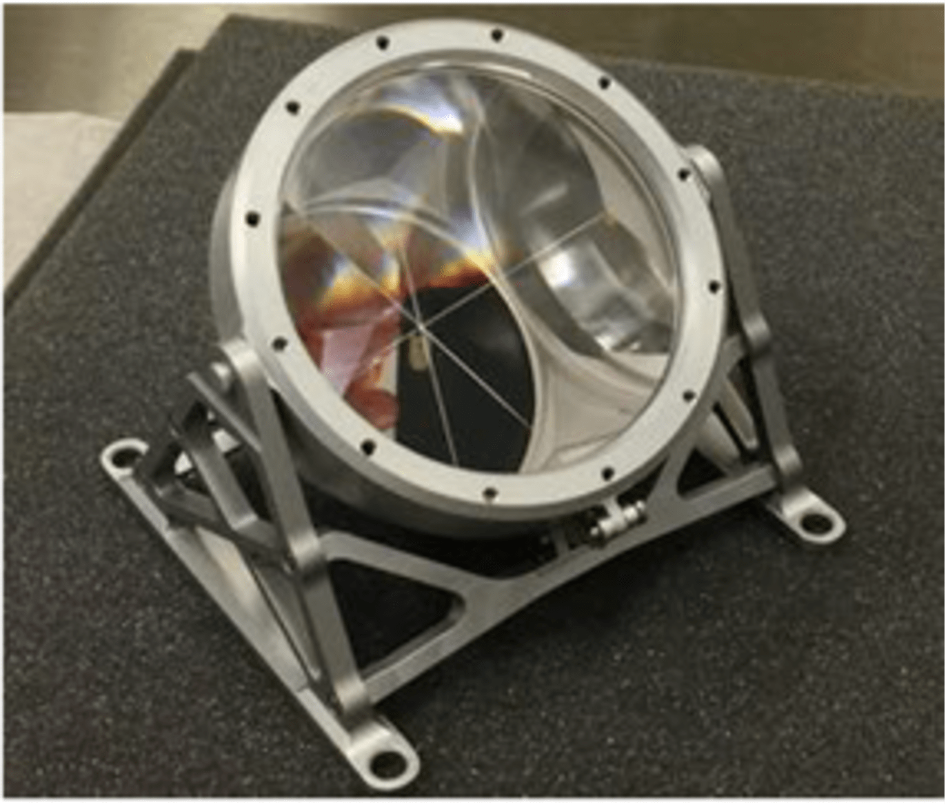 A hemisphere shaped payload has a connected stand. Its front face shines in the light while it rests on a black table.