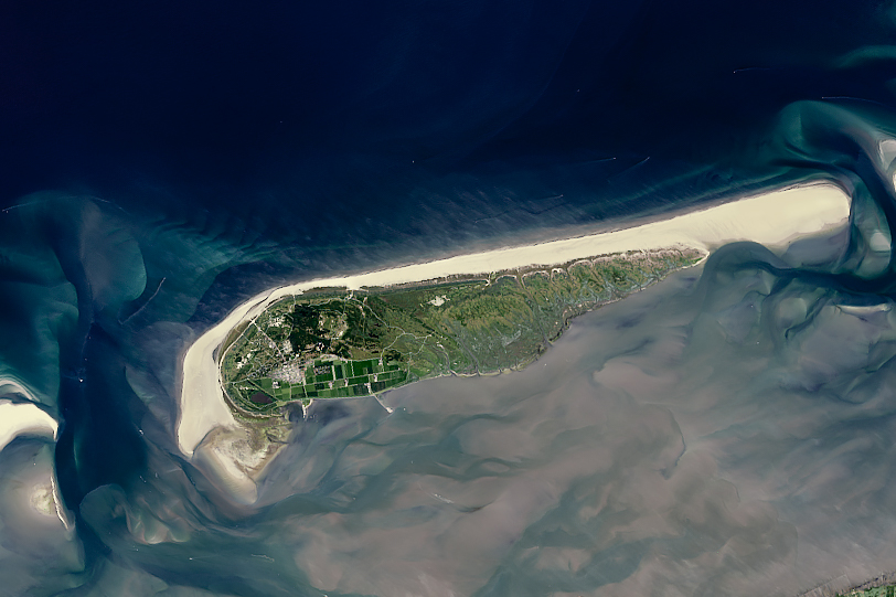 A sandy spit of land spans the majority of the image horizontally with breaks on both sides where the ocean, dark blue at the top of the image but heavily clouded with sediment below the island. The island, while having a sandy coast that borders the open ocean, has land with vegetation on the inland side and center, even seeming to include farmland.