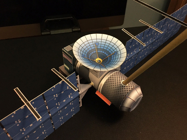 Image showing a paper model of Europa Clipper. The solar panels are blue, the high gain antenna is blue and yellow. The rest of the spacecraft is bronze.