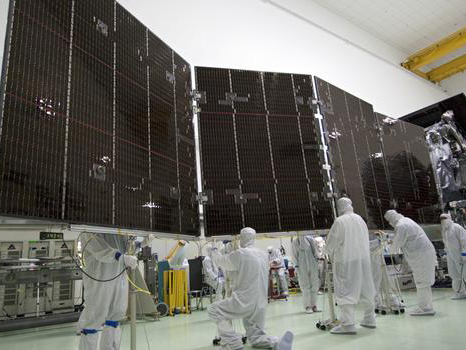 People in white protective clothing work around the solar panels for the Juno spacecraft.